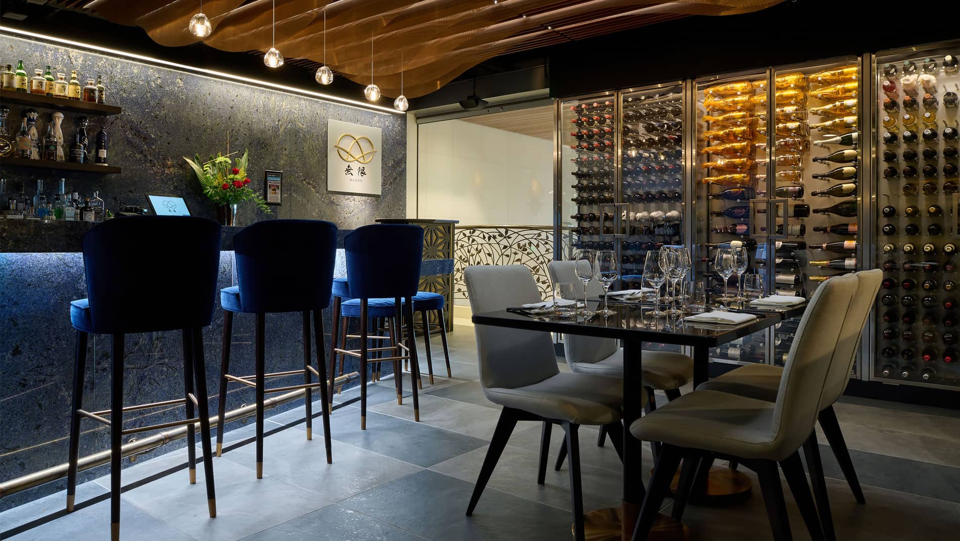 Dining room at Mugen, including a bar with cushioned tall chairs and a wall with a floor to ceiling wine display.
